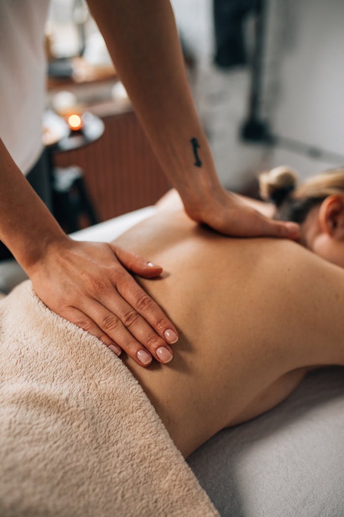 Close-up of hands massaging a person's back in a tranquil spa setting, promoting relaxation and wellness.